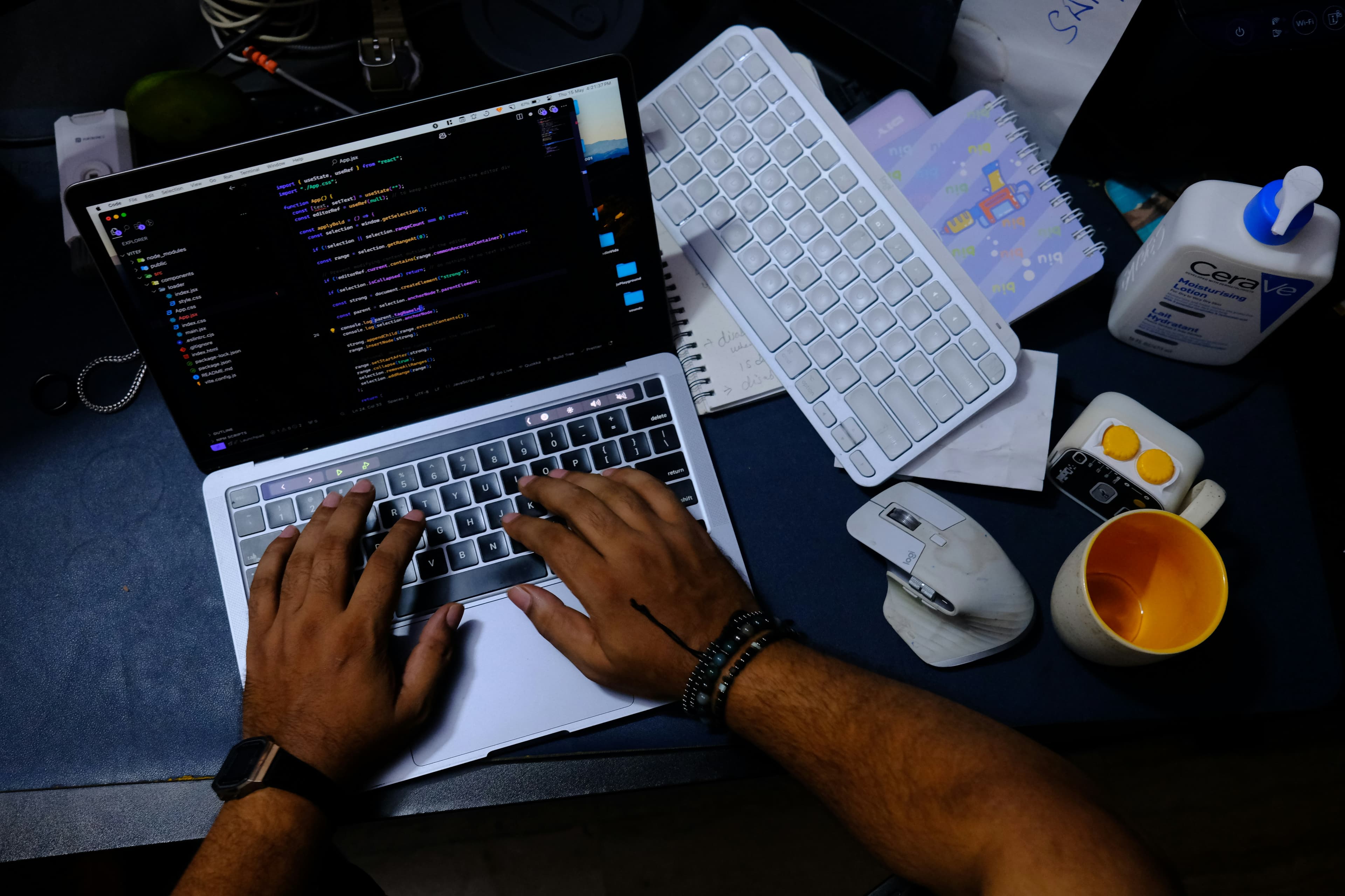 Close-up of hands typing on a laptop keyboard with lines of code visible on the screen, lit in cool blue and purple tones