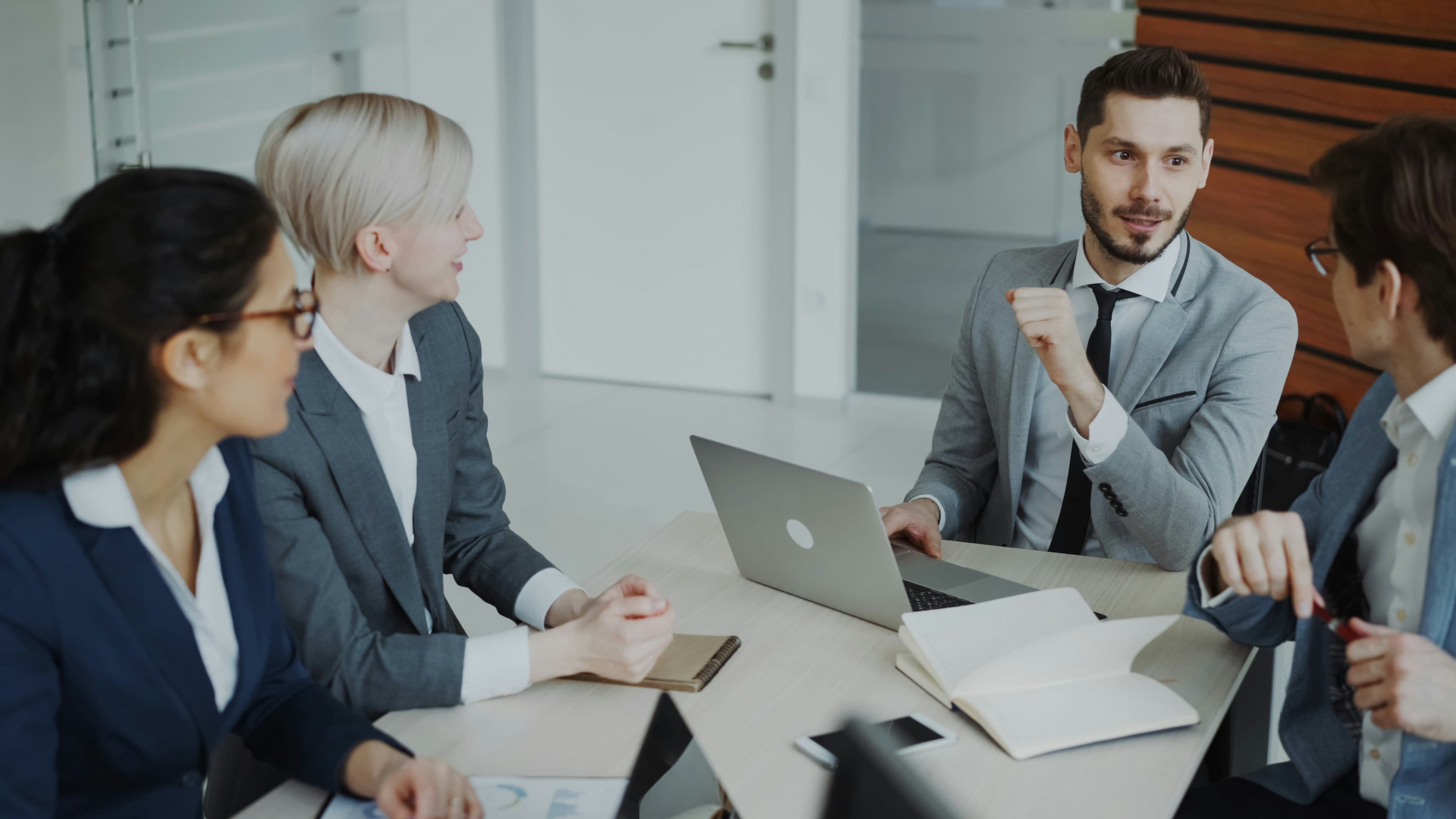 Four business professionals in formal attire reviewing documents and charts together at a conference table