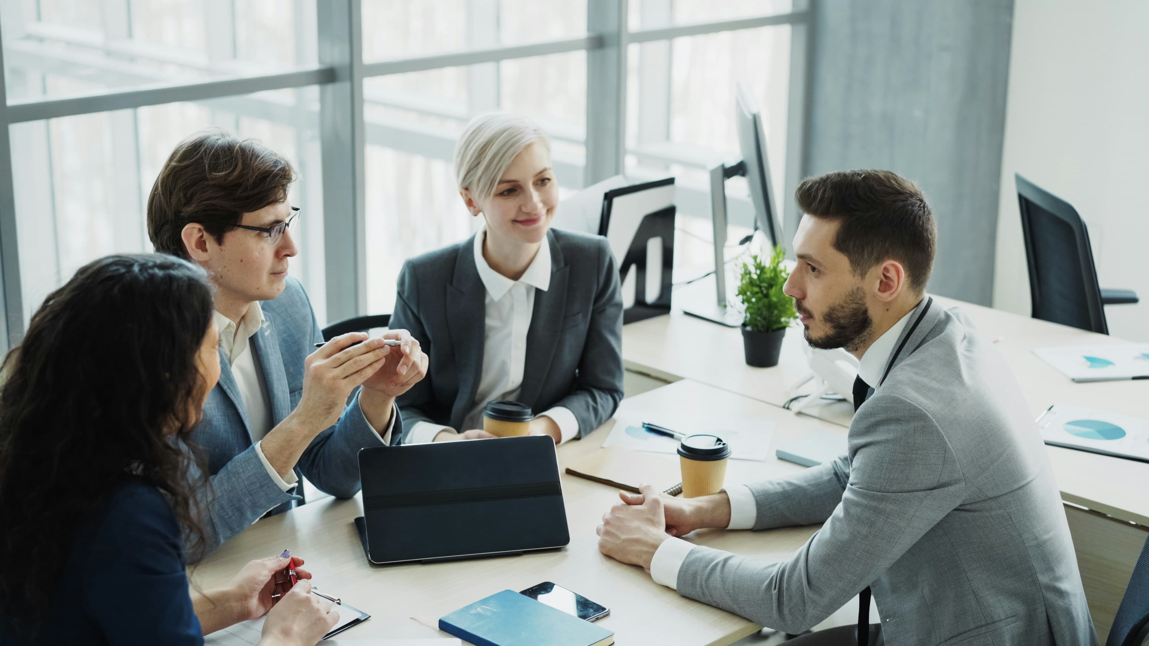 A team member in conversation with two colleagues at a table in a modern office, discussing a project