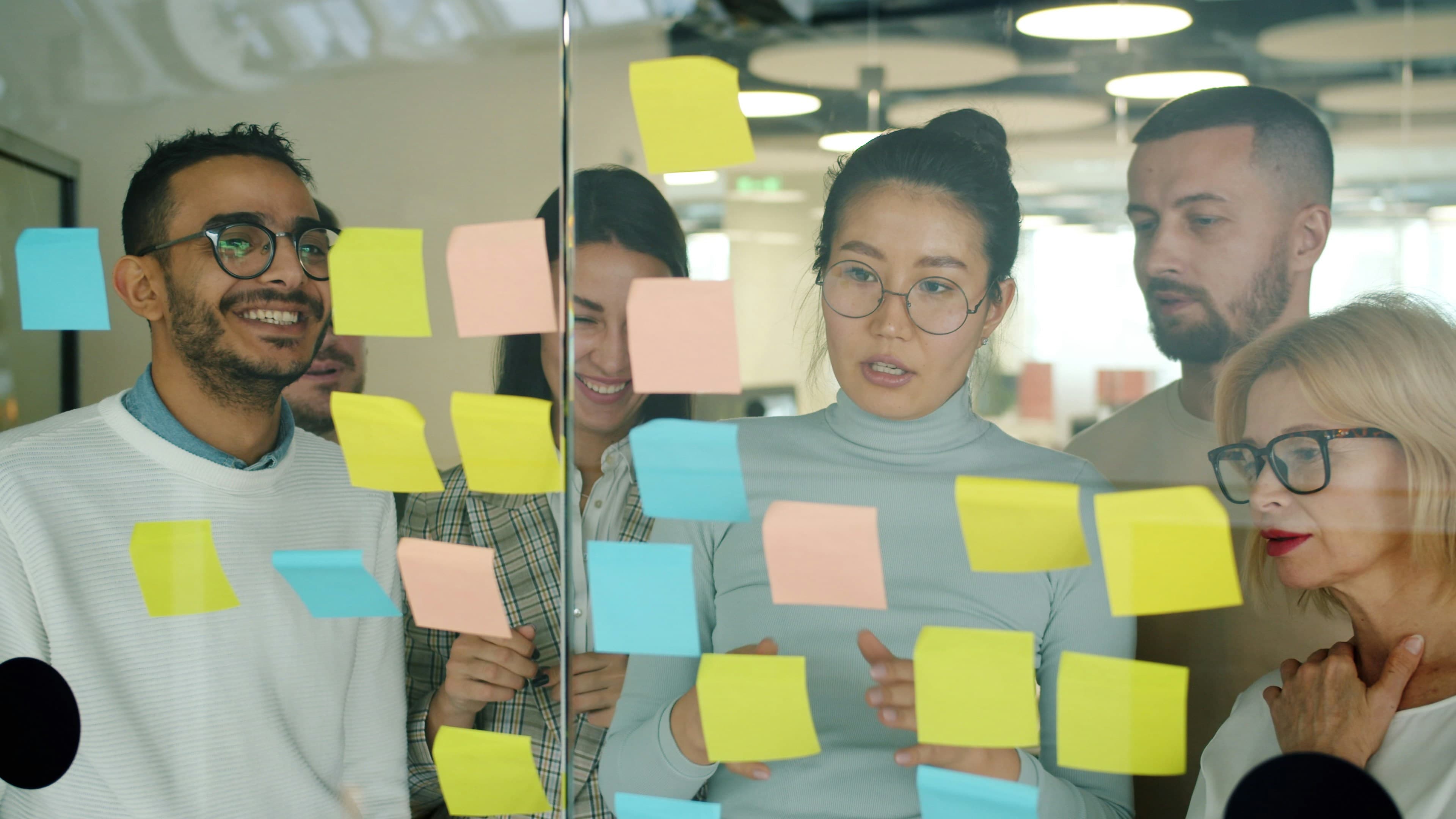 Colleagues laughing and discussing business strategy in front of a glass wall covered in colorful sticky notes
