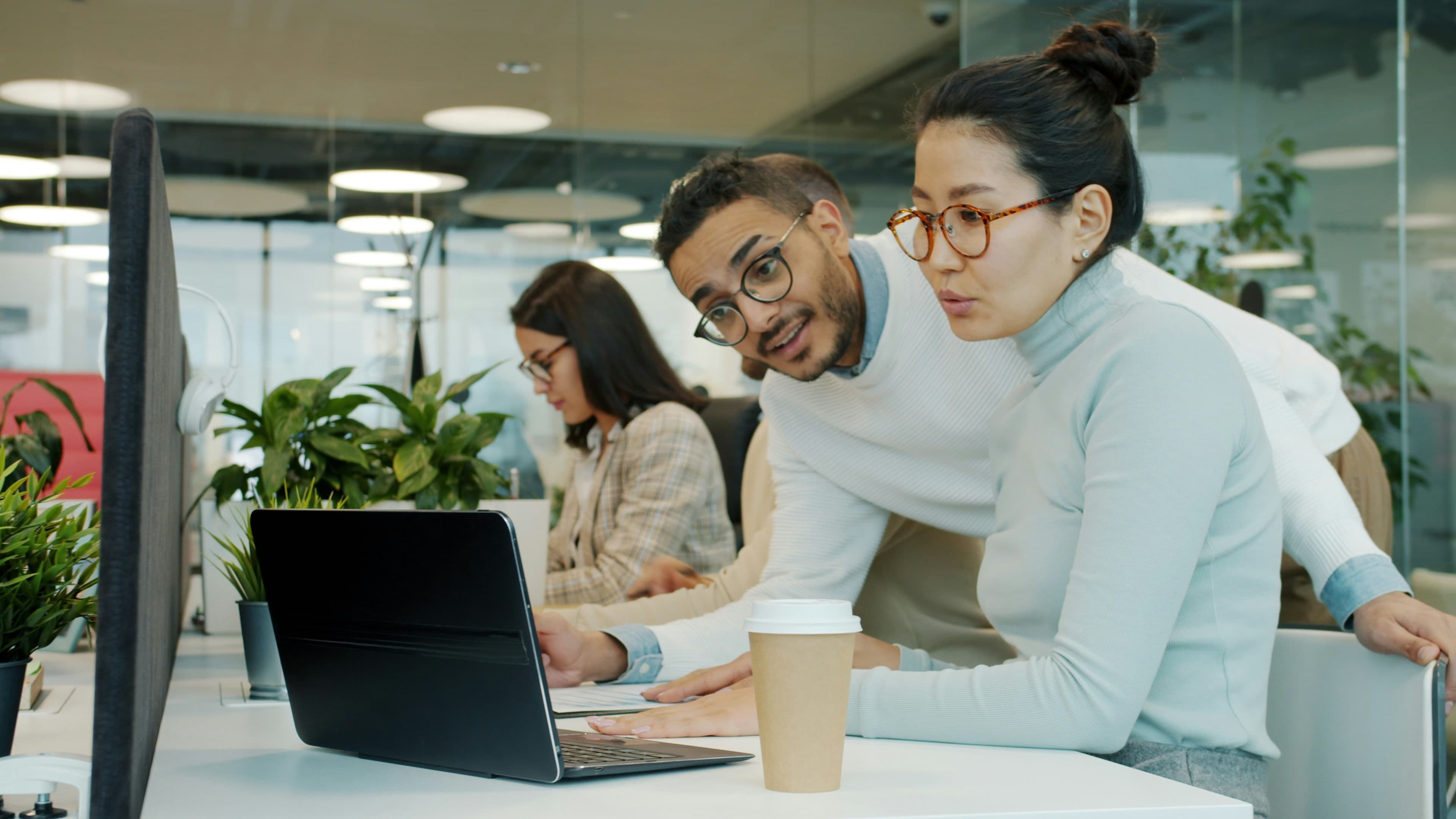 Two colleagues collaborating on a laptop in a shared office, discussing a screen together